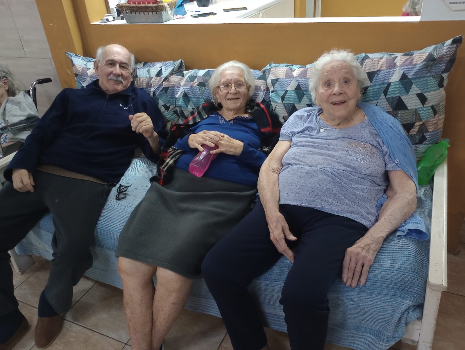 Tres personas comparten un momento en un sillón del hogar.