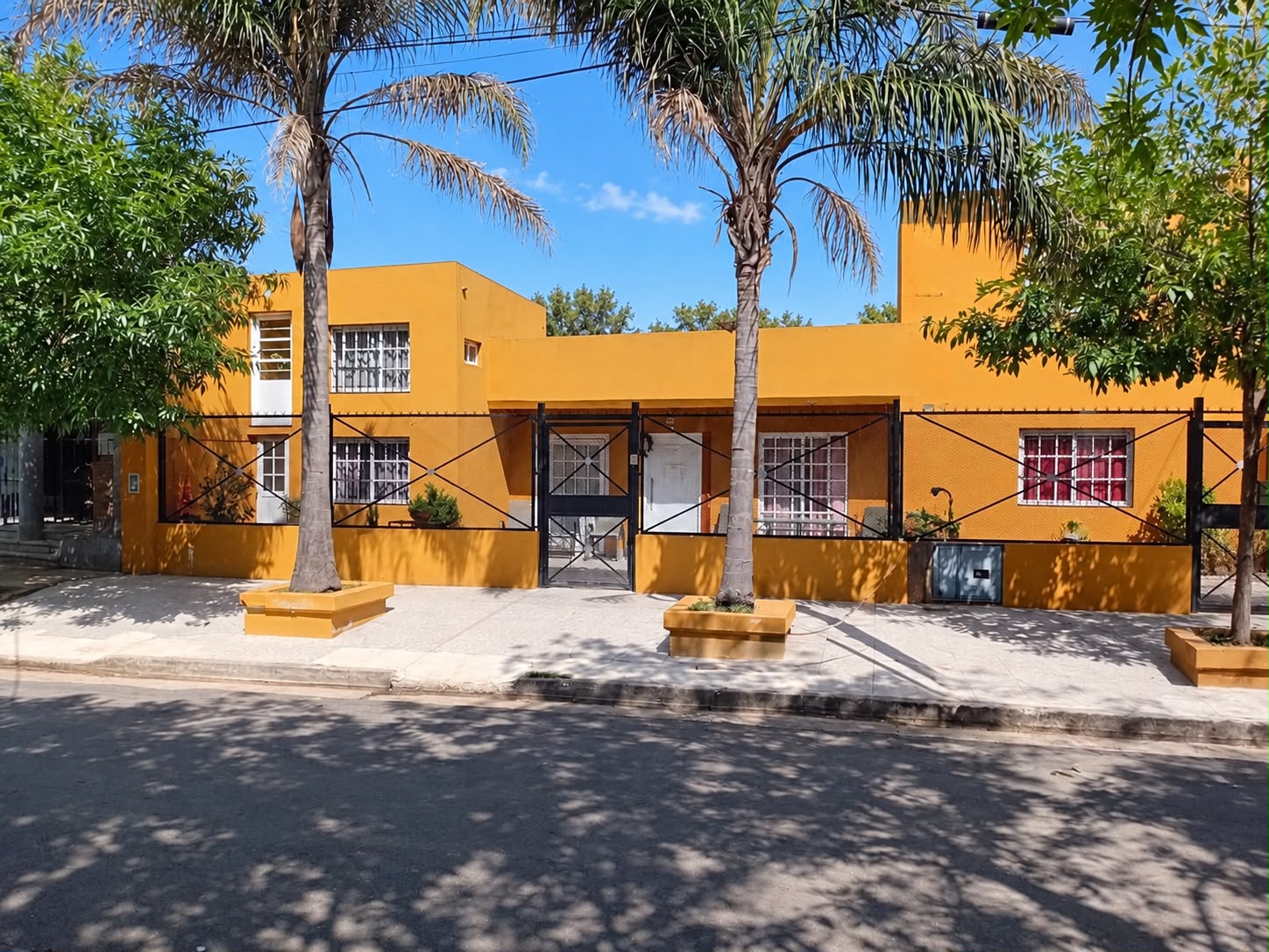 Fachada de Hogar Rucalaf, con paredes amarillas y palmeras frente a la entrada.
